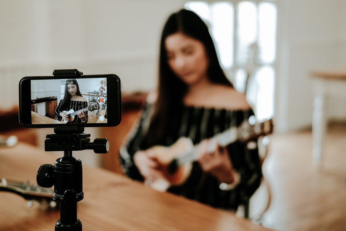 A musician recording herself on a phone mounted on a tripod